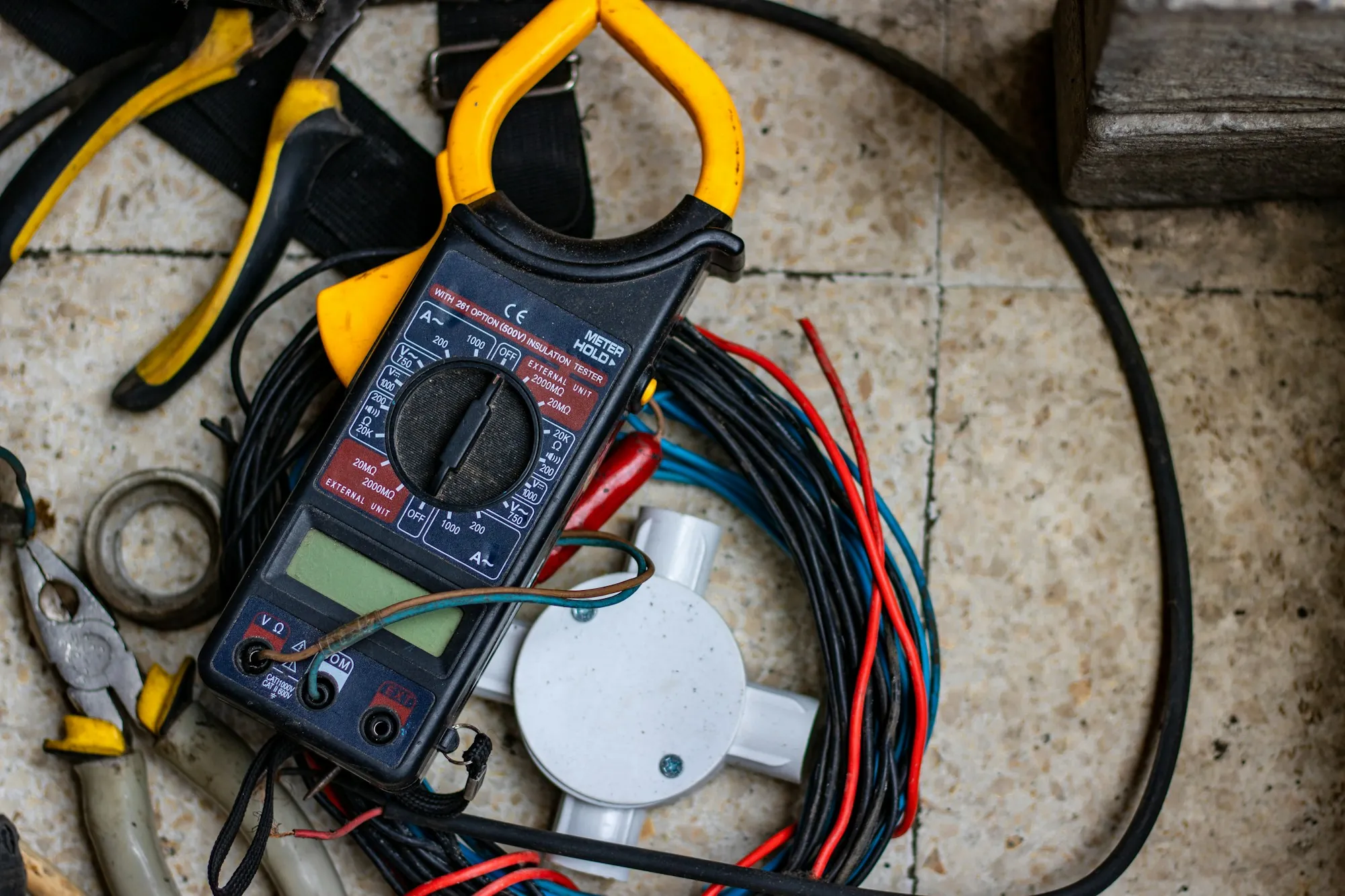 A multimeter and hand tools beside coiled electrical cable